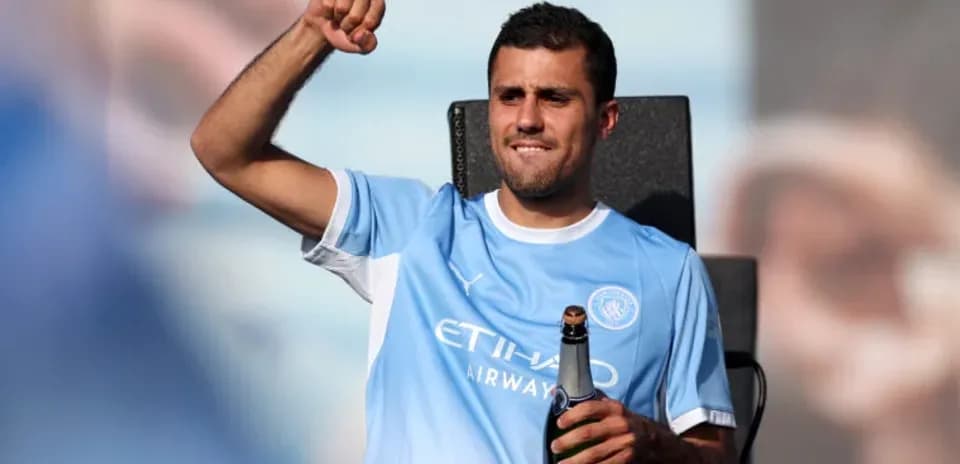 Futbolchi shampan bilan sahnada turib qo'lini ko'taradi