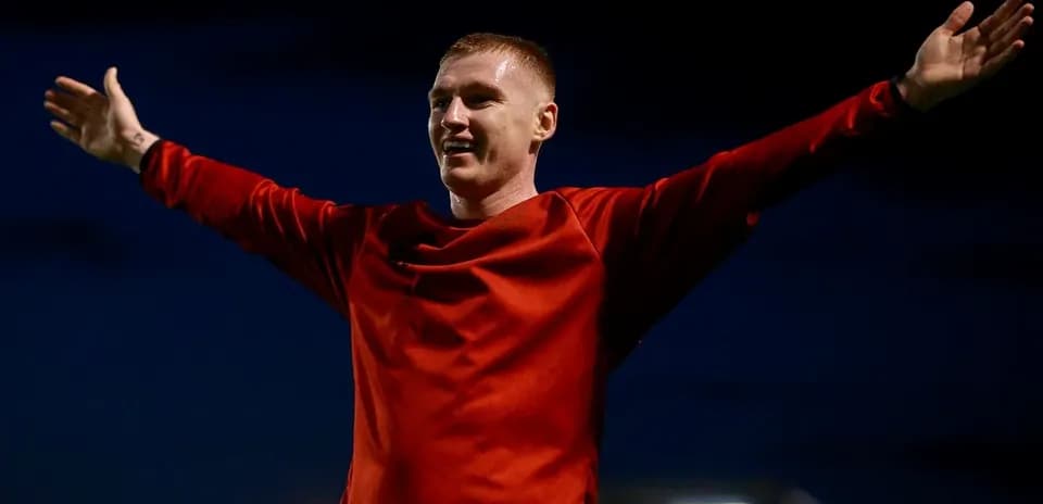Futbolchi qizil forma kiyib, qulog'ini ochib turibdi