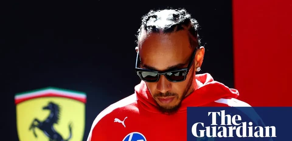 Driver in red attire walking past Ferrari logo