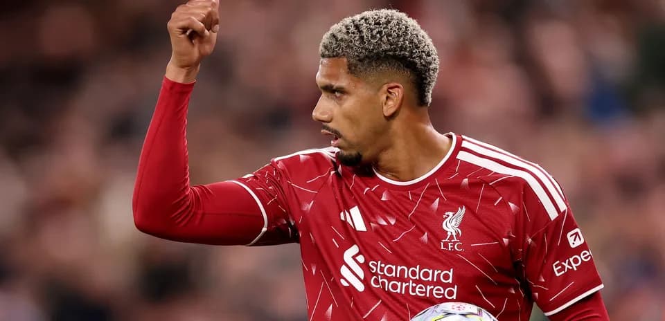 Futbolchi LFC formasida, qo'lini ko'tarib turibdi