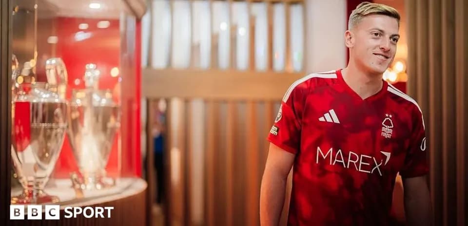 Futbolchi qizil formada, kuboklar oldida turibdi
