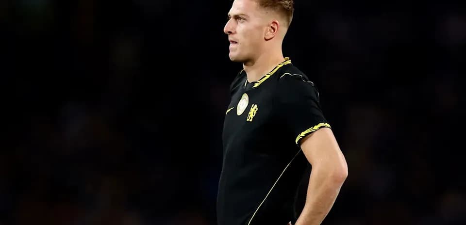 Futbolchi qora formada, maydon bo'yida turibdi