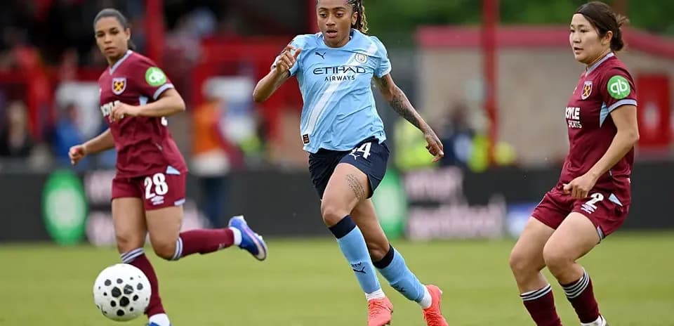 Manchester City player dribbling past West Ham defenders