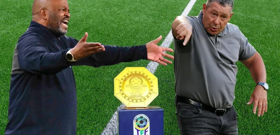 Two coaches gesturing beside a trophy on field