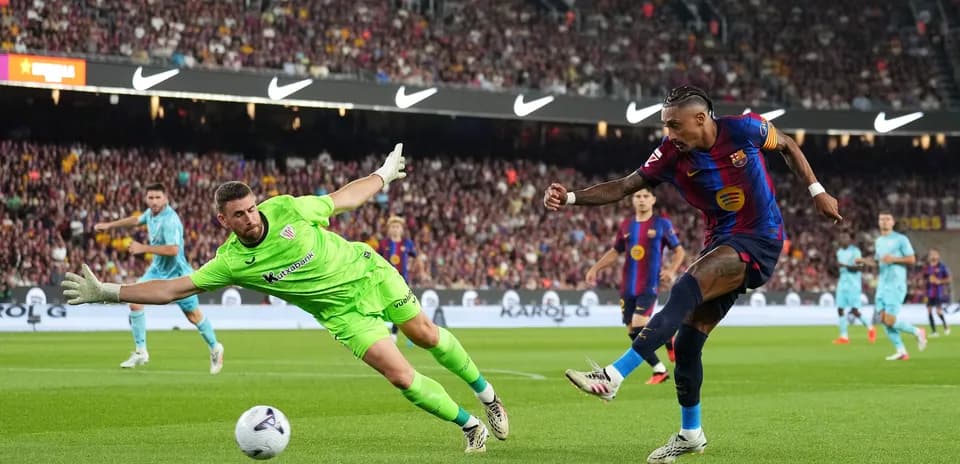Barcelona player shooting as goalkeeper dives for ball