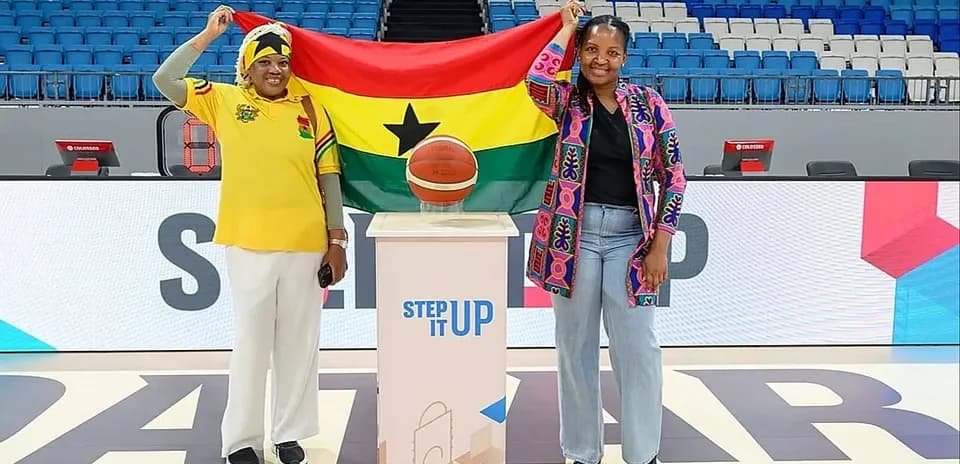Two women holding Ghana flag with basketball on podium