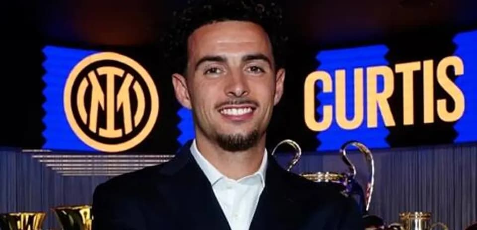 Football player posing with trophies and club logo