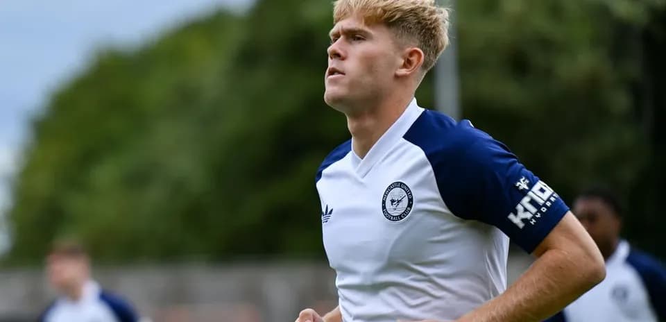 Futbolchi mashg'ulotda yugurmoqda, maydon orqa fonda