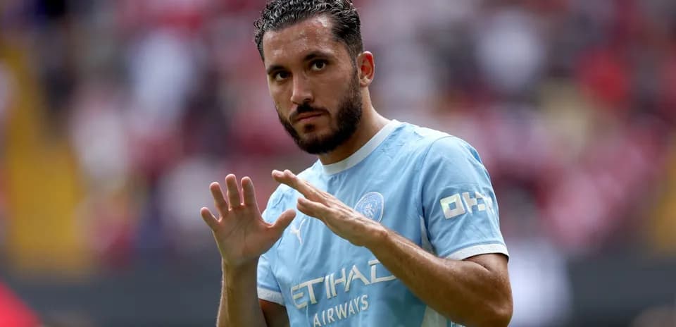Futbolchi maydonda qo'llarini ko'tarib turibdi