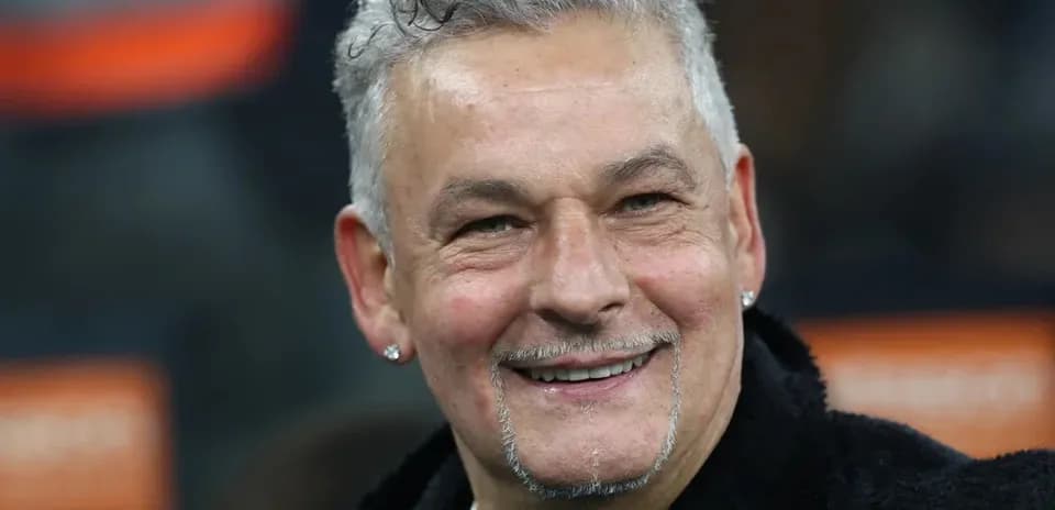 Man with curly hair and earrings smiling