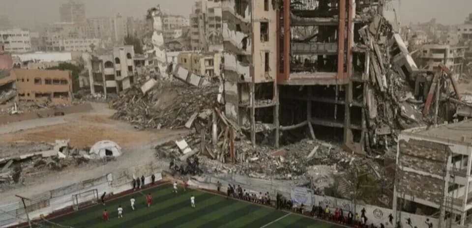 Football match taking place near destroyed buildings