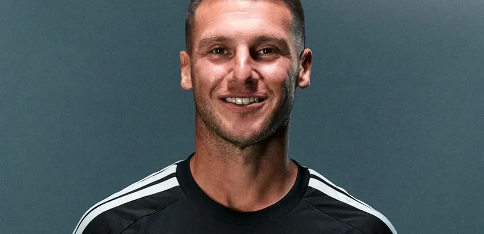 Futbolchi qora forma kiygan, tabassum qilmoqda