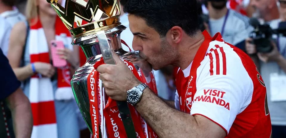 Mikel Arteta kissing Premier League trophy on stage