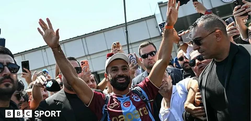 Futbolchi muxlislar orasida qo'lini ko'tarib turibdi