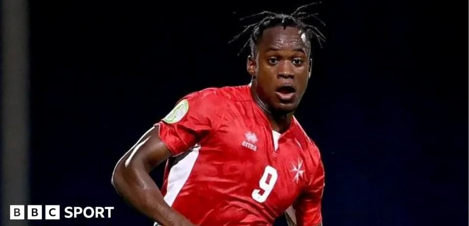 Futbolchi raqibga qarshi harakatda, qizil forma kiygan
