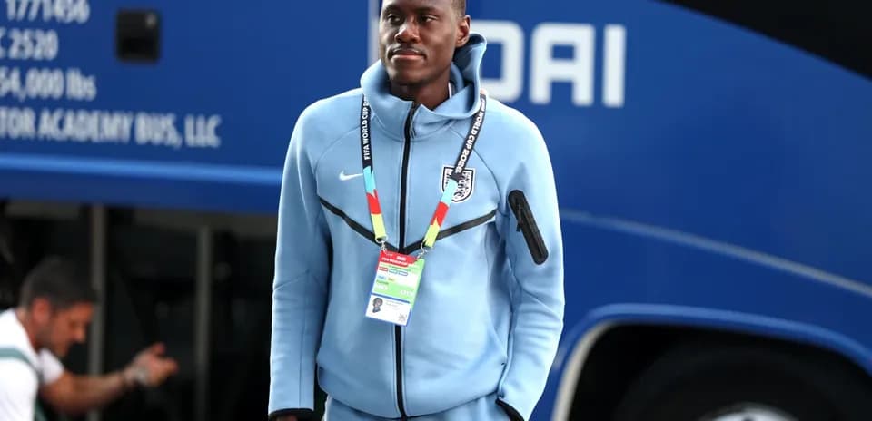 Futbolchi avtobus oldida ko'k kiyimda turibdi