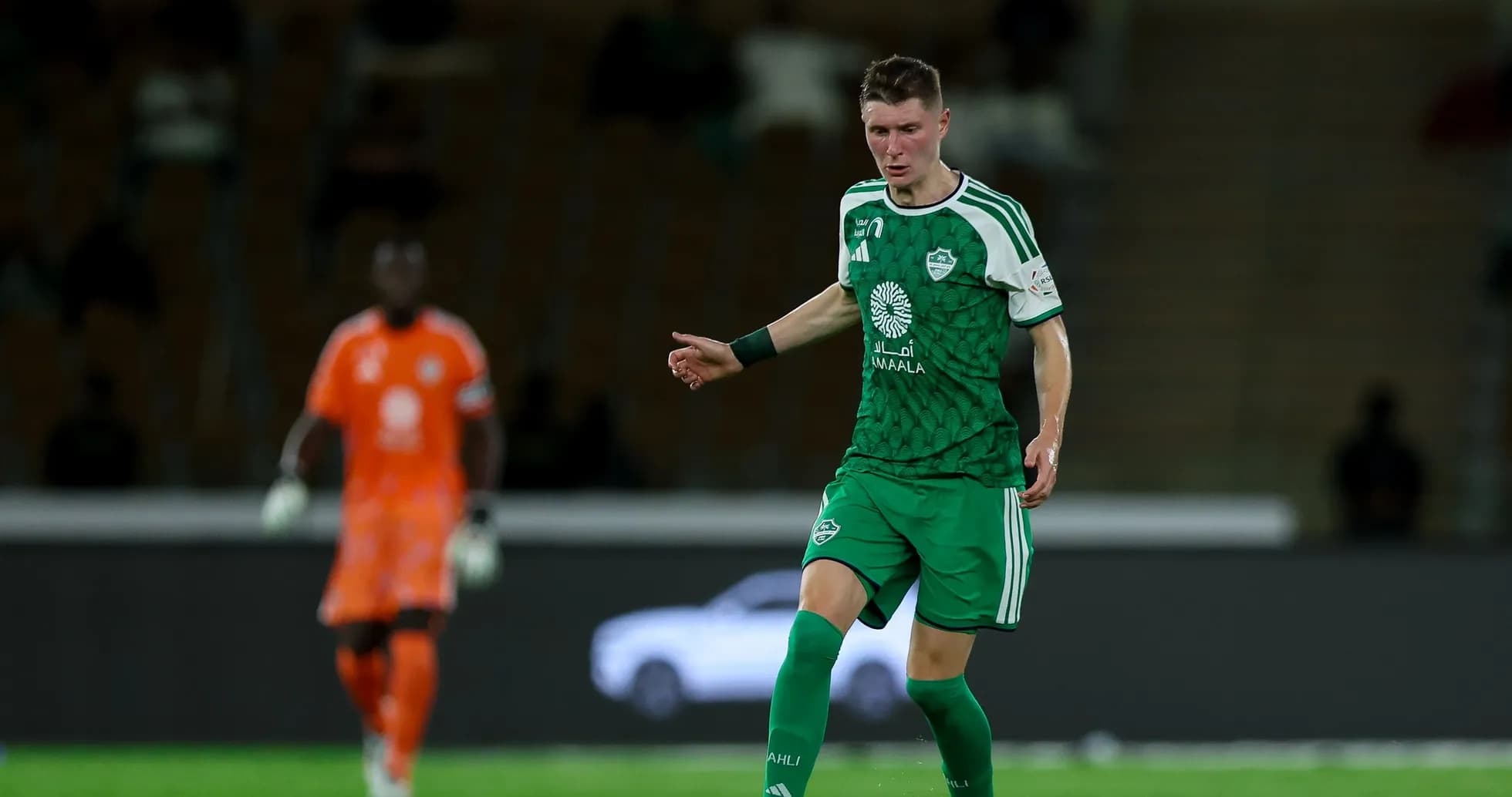 Futbolchi to'pni nazorat qilmoqda, darvozabon orqa planda Futbolchi to'pni nazorat qilmoqda, darvozabon orqa planda
