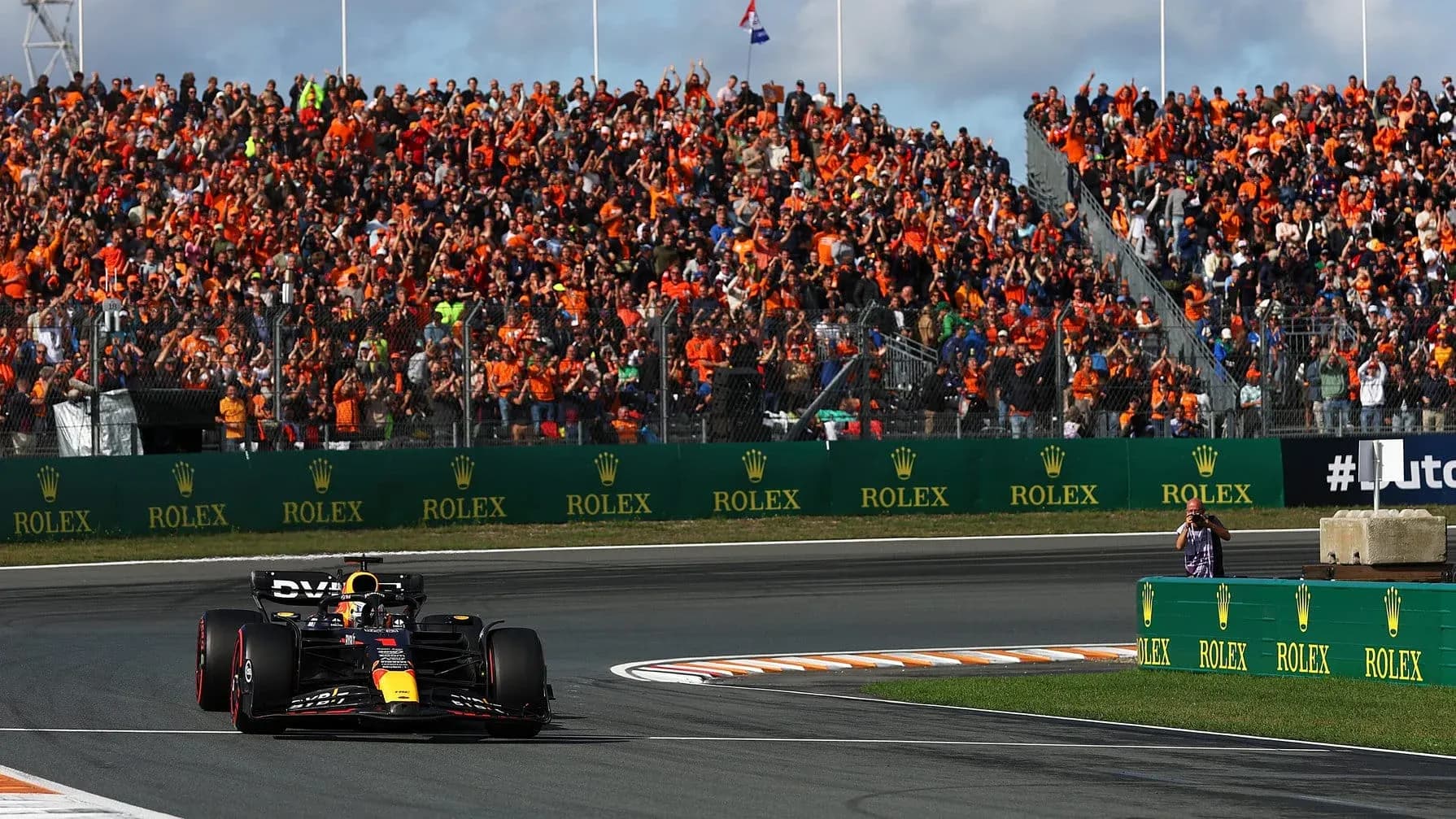 Formula 1 car racing past cheering crowd in orange Formula 1 car racing past cheering crowd in orange