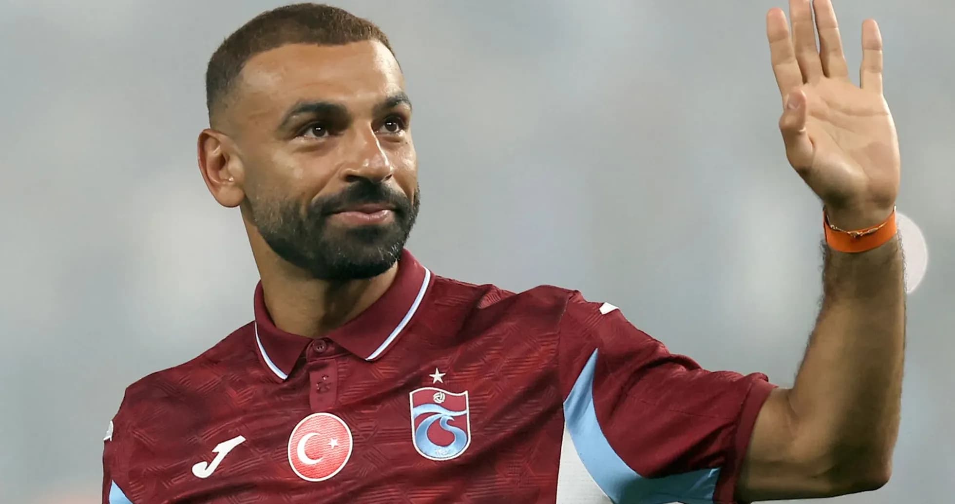 Futbolchi qo'lini ko'tarib muxlislarga salom berayapti Futbolchi qo'lini ko'tarib muxlislarga salom berayapti